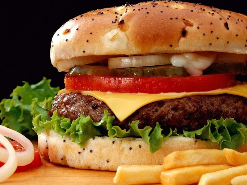 A burger with French fries and tomatoes with onions on the side