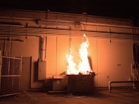 A dumpster fire roaring in front of a building