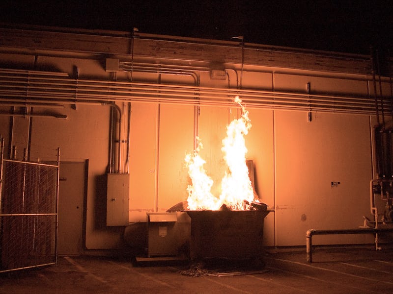 A dumpster fire roaring in front of a building