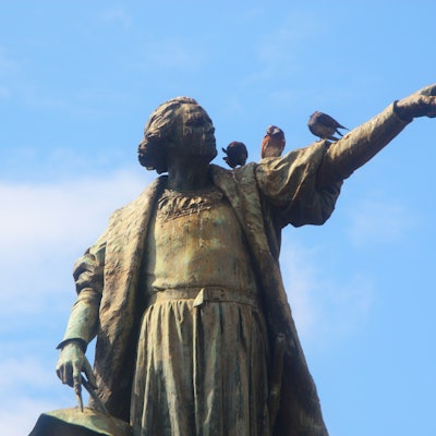 A statue of Christopher Columbus with birds sitting on its arm