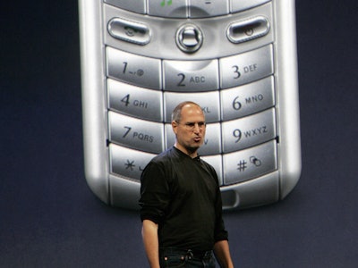 Steve Jobs presenting in front of an enlarged photo of a cell phone