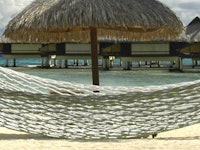 A hammock in the foreground with a palm beach umbrella stuck in the water