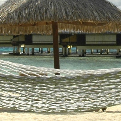 A hammock in the foreground with a palm beach umbrella stuck in the water