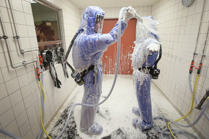 Two people in blue protective suits and masks cleaning themselves due to the risk of contracting Ebo...