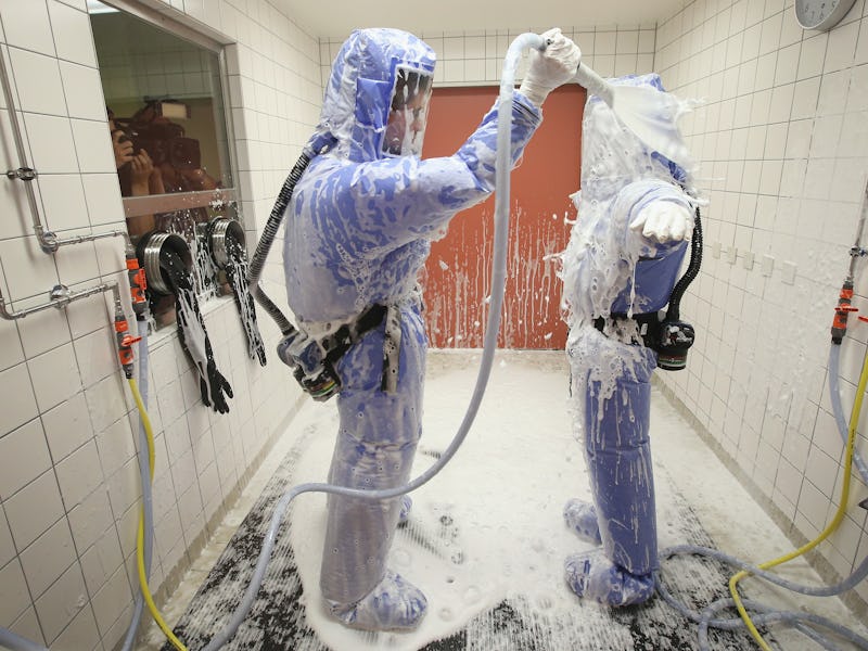 Two people in blue protective suits and masks cleaning themselves due to the risk of contracting Ebo...