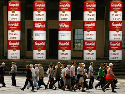 A group of pedestrians walking with several Campbell Soup’s Wet Noodle ad poster on a wall on the bu...