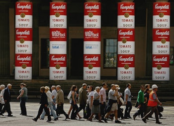 A group of pedestrians walking with several Campbell Soup’s Wet Noodle ad poster on a wall on the bu...