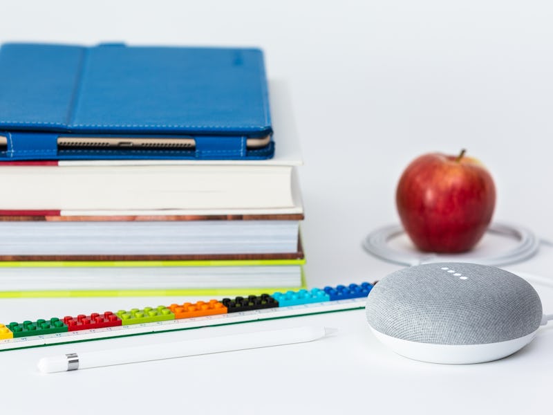 A portable white speaker, an apple, three notebooks, and a tablet on a white surface