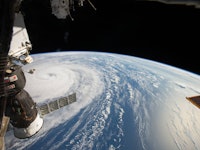 An aerial view of planet Earth near a satellite and Typhoon Noru on the surface