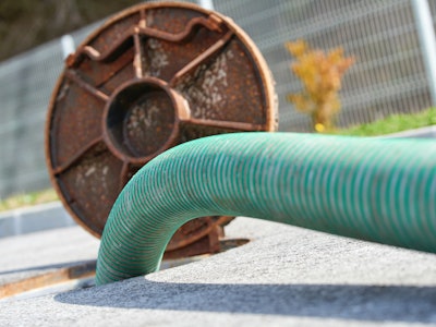 A green plastic pipe inserted into an open sewage