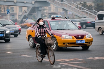 Woman with protective mask rides bike on a busy street in Dongcheng District in Beijing