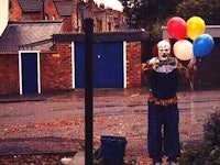 A rampant clown holding balloons standing in the middle of a street