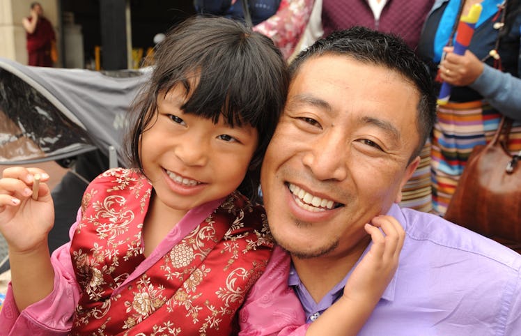 Tibetan girl in a red & gold silk chuba / pink blouse, her daddy in a purple cotton shirt, woman hol...