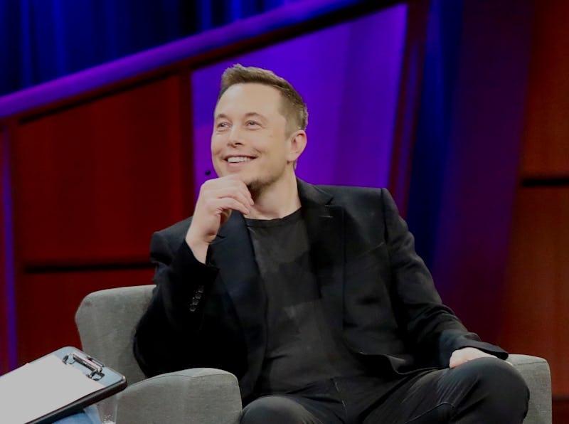 Elon Musk smiling in a black shirt and black blazer during an interview 