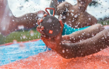 A boy holding a JBL Clip-On bluetooth speaker while playing in a pool