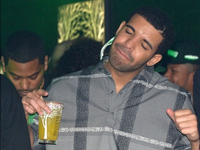 Drake dancing with his eyes closed while holding one of the drinks he has rapped about 