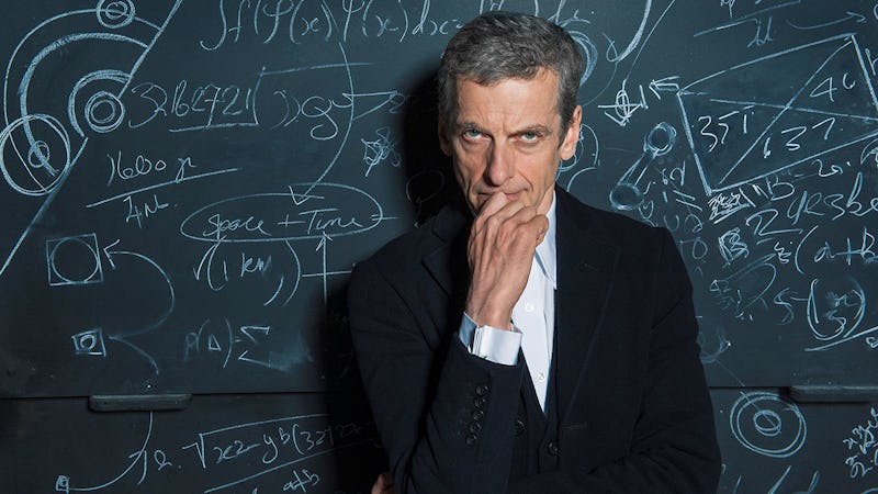 Peter Capaldi in a white shirt and black blazer in front of a blackboard