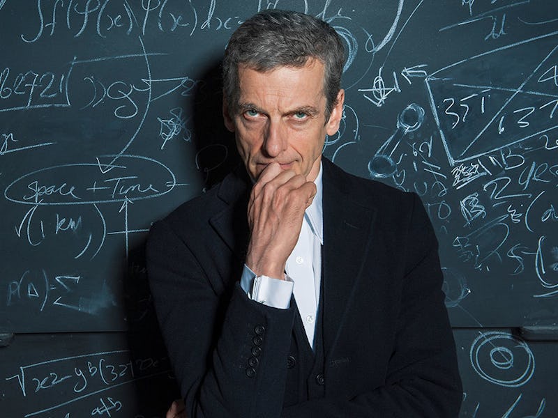 Peter Capaldi in a white shirt and black blazer in front of a blackboard