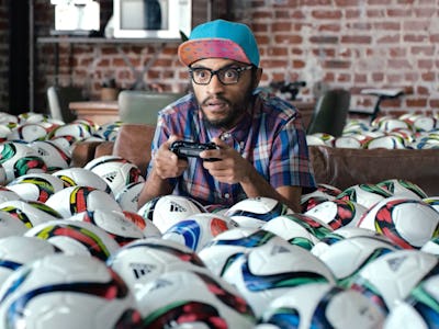 A man focused on playing video games on PlayStation in a room filled with soccer balls