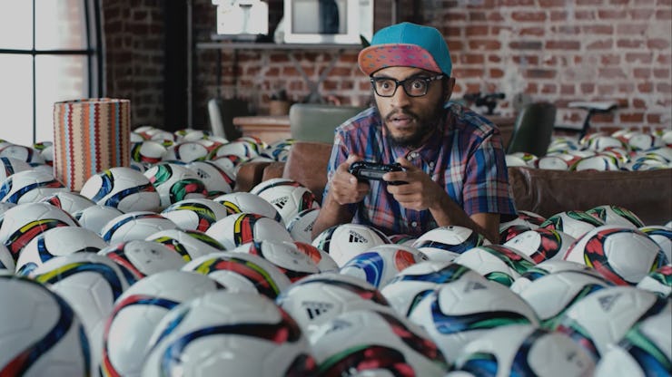 A man focused on playing video games on PlayStation in a room filled with soccer balls