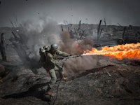 A battle scene screenshot from 'Hacksaw Ridge' with a character using a flamethrower 