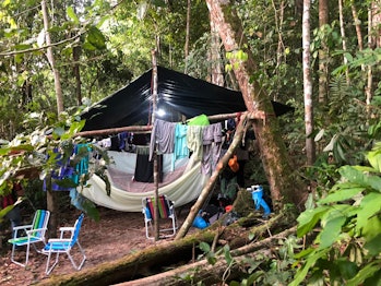 a tent in the woods surrounded by clothes on clotheslines 