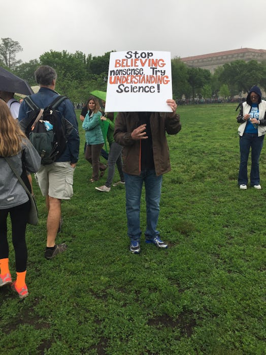 A man holding a poster with "stop believing nonsense, try believing science" text