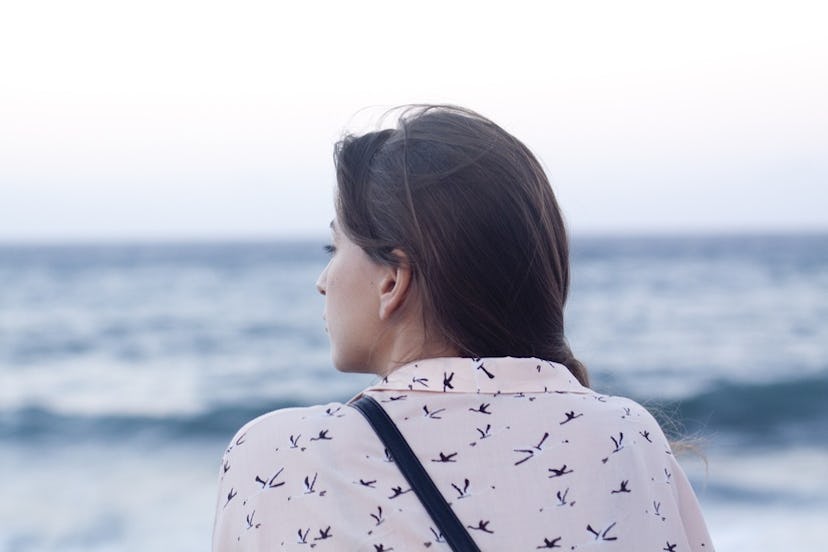 A woman in a white floral shirt looking at the waves of a sea nearby