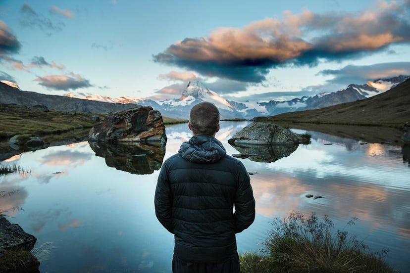 A man in a black hooded jacket looking at a lake in the distance