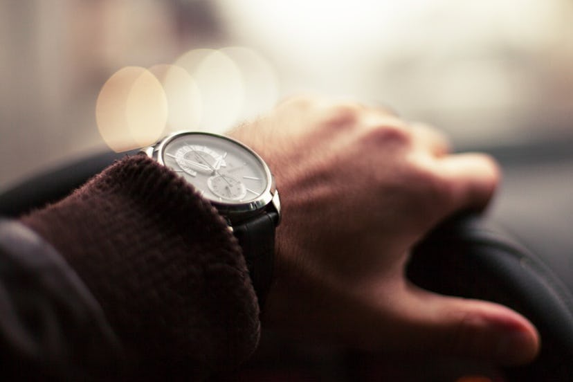 A man's hand with a watch on a car's steering wheel