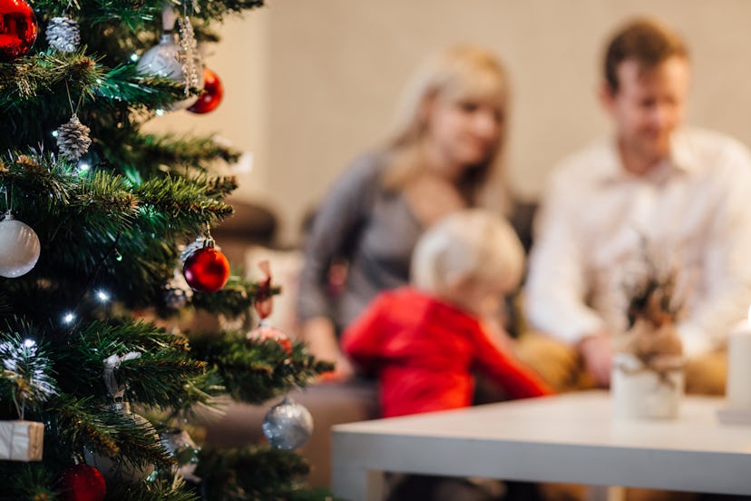Parents with their blonde toddler blurred in the background of a Christmas tree
