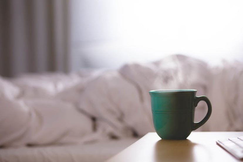 Green and hot cup of coffee next to a bed  with someone sleeping in it