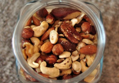 A close-up, overhead view of a clear jar filled with a variety of mixed nuts, including cashews, almonds, and pecans.