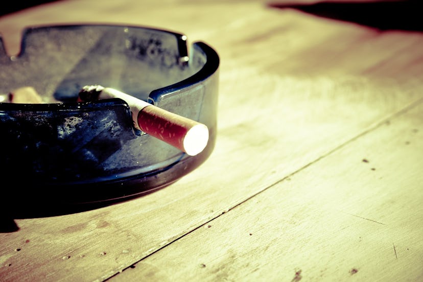 An ashtray on a wooden surface with a lit cigarette placed inside of it which can hurt your immune s...