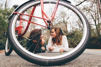 Two female friends lying on the road and talking behind the bicycle wheel.