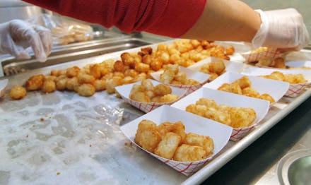 A person serving fast food potatoes in white boxes for students