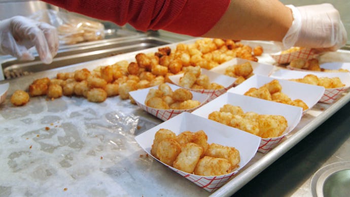 A person serving fast food potatoes in white boxes for students