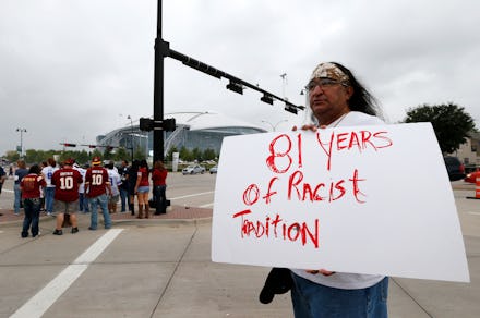 A man standing in a parking lot holding a white poster with red text '81 years of racist tradition'