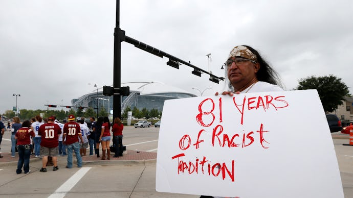 A man standing in a parking lot holding a white poster with red text '81 years of racist tradition'
