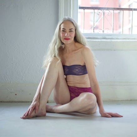 A blonde lady posing for a photo on the floor of her home in a bra