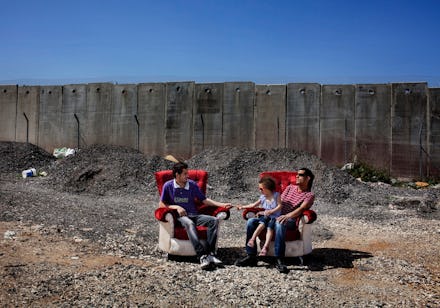 Two Palestinian men sitting in red armchairs on an abandoned lot