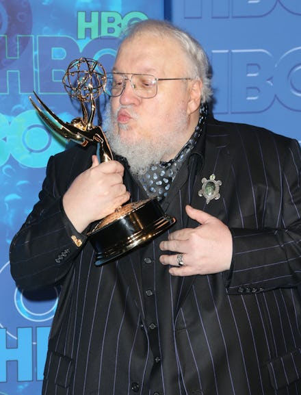 George R. R. Martin holding and kissing his Emmy award statue in a striped black suit
