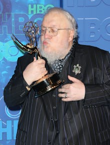 George R. R. Martin holding and kissing his Emmy award statue in a striped black suit