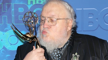 George R. R. Martin holding and kissing his Emmy award statue in a striped black suit