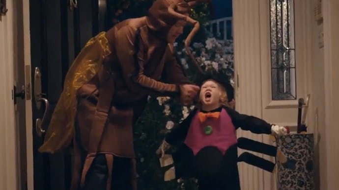 A dad dressed as a cockroach adjusting the spider costume of a child in their home