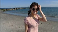 Lihuan Wang in a dress and sunglasses posing on the beach, smiling