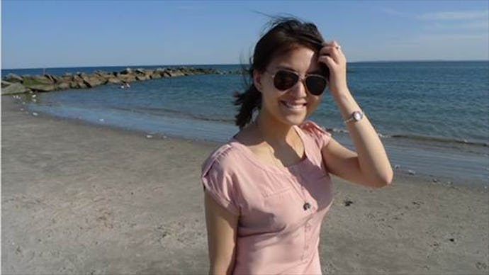 Lihuan Wang in a dress and sunglasses posing on the beach, smiling