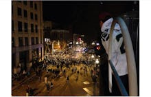 Super Bowl fans gathered around at night, and a man watching them from a balcony. 