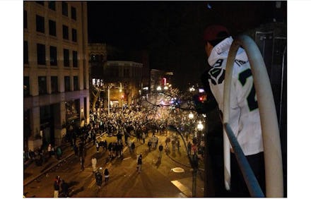 Super Bowl fans gathered around at night, and a man watching them from a balcony.