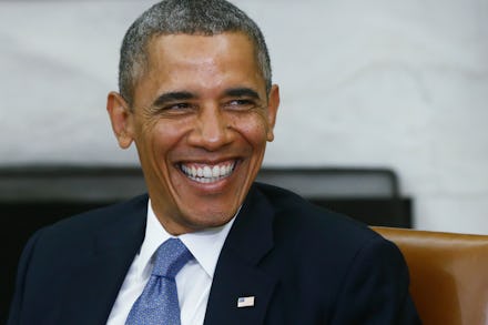 Barack Obama laughing in a black suit, white shirt and blue tie